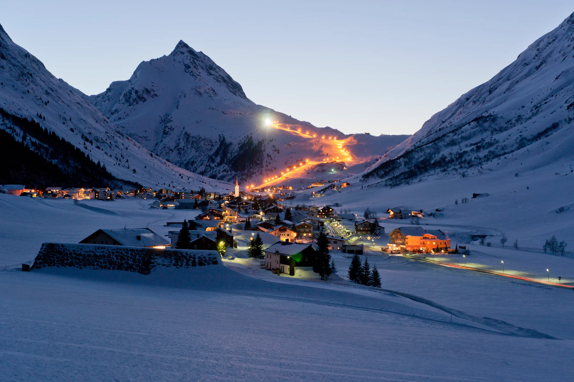 Verschneites Galtür mit beleuchteten Häusern und Bergen in der Abenddämmerung